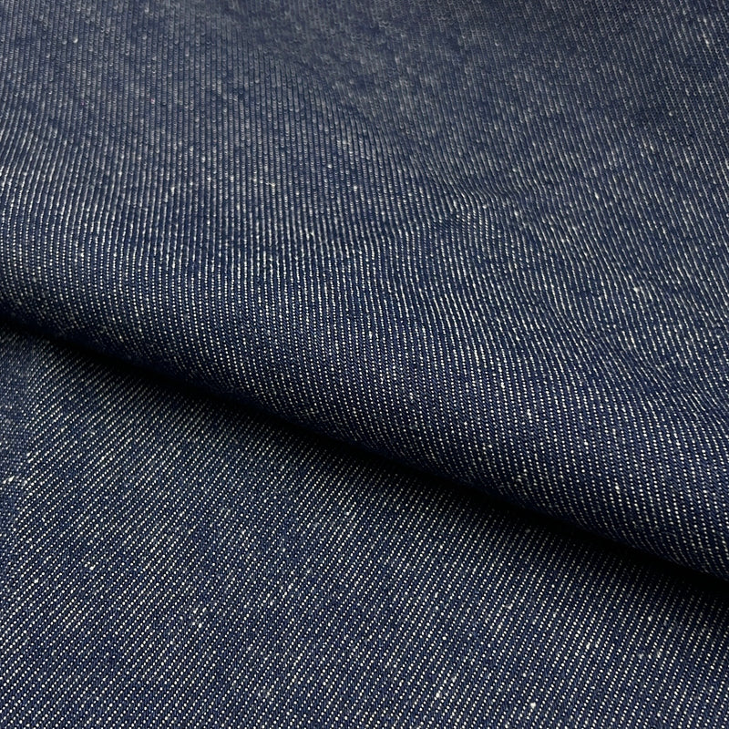 A close-up of dark indigo denim fabric with a diagonal fold showing the textured twill weave.