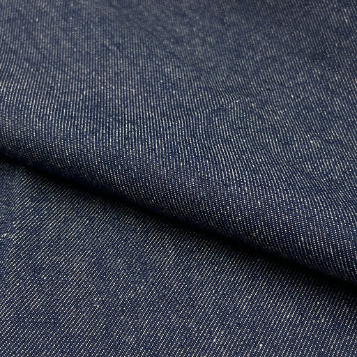 A close-up of dark indigo denim fabric with a diagonal fold showing the textured twill weave.