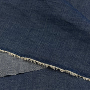 A close-up of dark indigo denim fabric with a frayed cut edge showing the lighter inner weave.