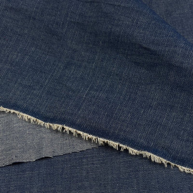A close-up of dark indigo denim fabric with a frayed cut edge showing the lighter inner weave.