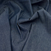 A close-up of draped slate blue fabric with a visible woven texture, showing soft folds and shadows.