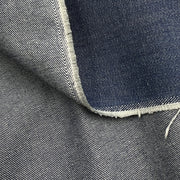 Close-up of a folded piece of dark indigo denim fabric showing the blue weave and white raw frayed edges.