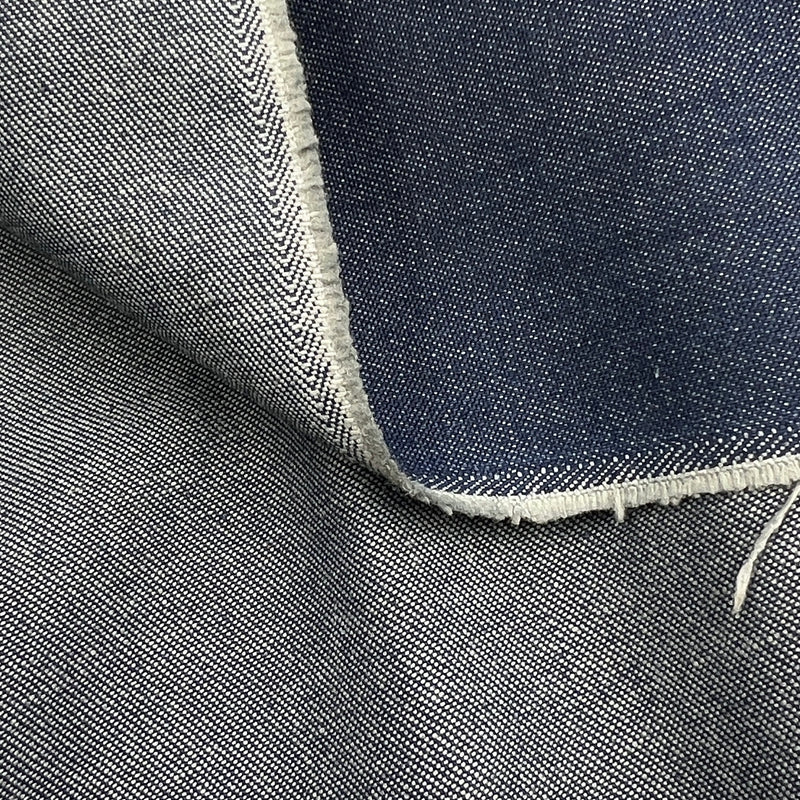 Close-up of a folded piece of dark indigo denim fabric showing the blue weave and white raw frayed edges.