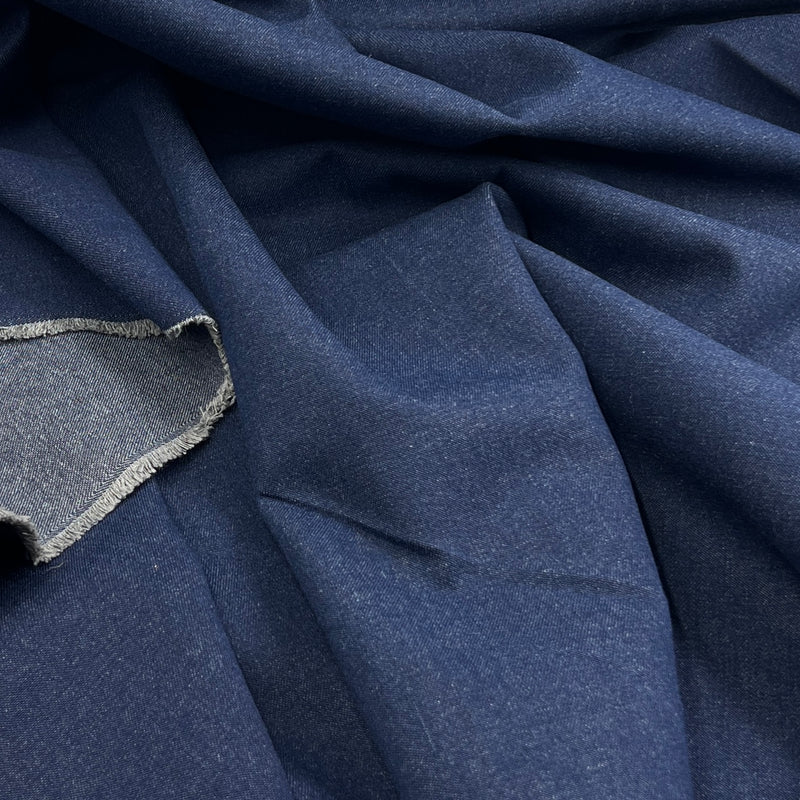 A close-up of draped navy blue fabric with a visible woven edge and a small fabric sample shown in the lower left corner.