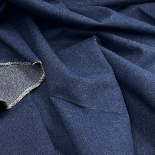 A close-up of draped navy blue fabric with a visible woven edge and a small fabric sample shown in the lower left corner.