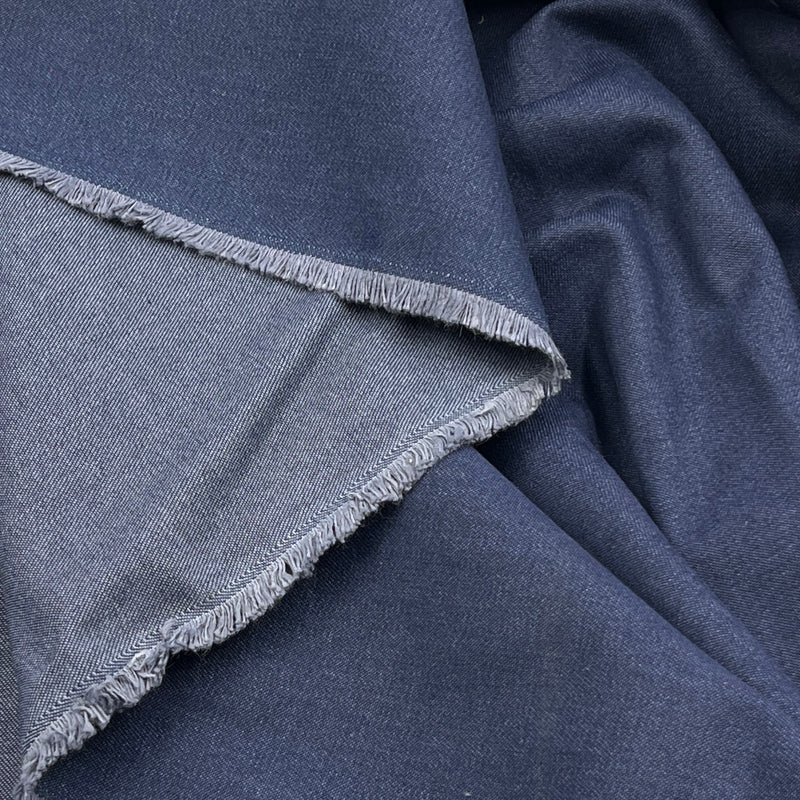A close-up of folded dark blue fabric with a visible lighter blue frayed edge, showing the material texture and color variation.