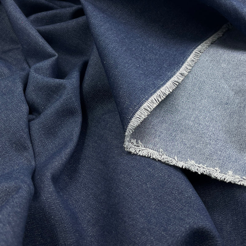A close-up of dark blue fabric with a visible light blue reverse side and frayed selvedge edge, draped to show texture and weave.