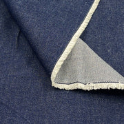 A close-up of dark blue denim fabric with a folded corner showing a light beige frayed edge.