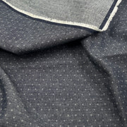 A close-up of dark gray fabric with a small white geometric dot pattern and a folded hem showing a white frayed edge.