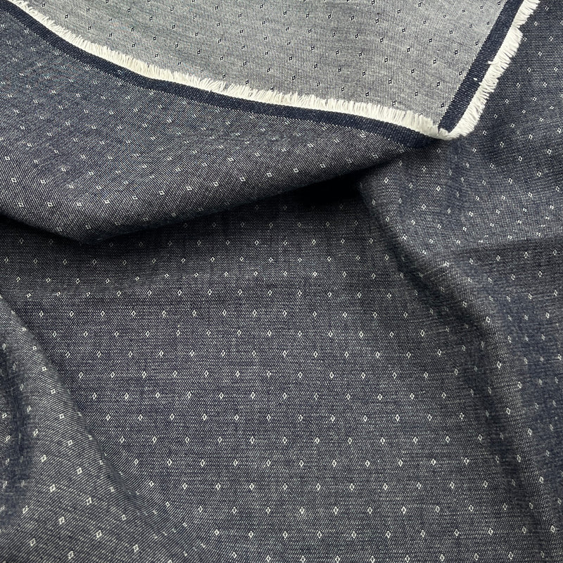 A close-up of dark gray fabric with a small white geometric dot pattern and a folded hem showing a white frayed edge.