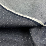 A close-up of folded dark gray fabric with a small repeating white geometric pattern and a contrasting white frayed edge.