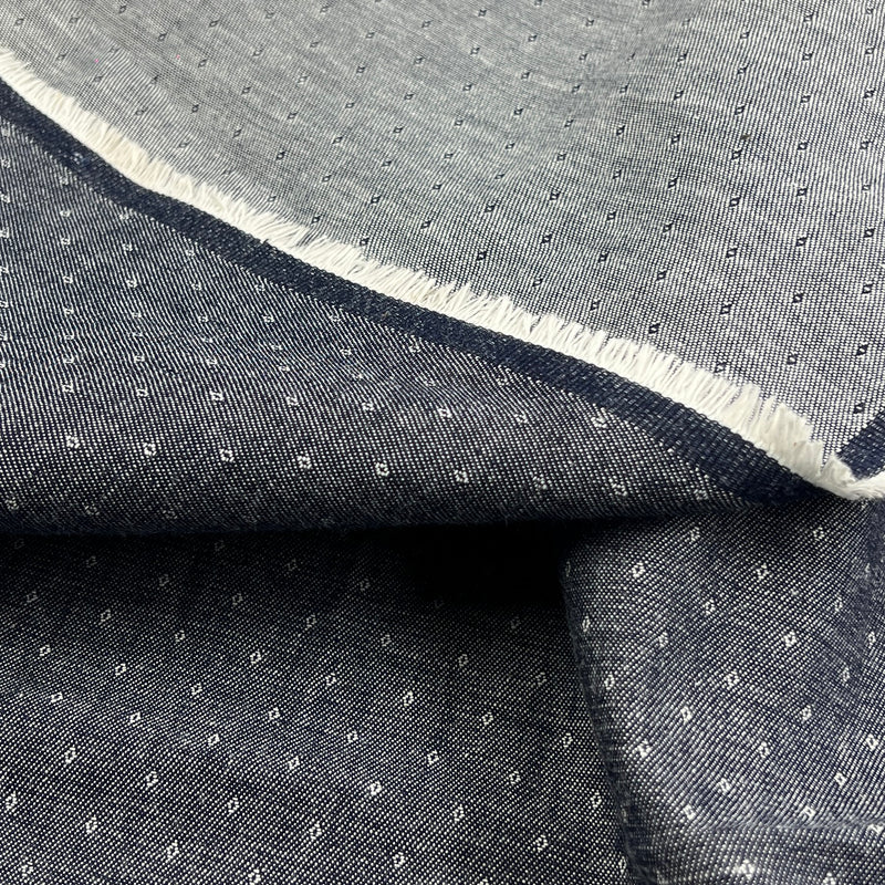 A close-up of folded dark gray fabric with a small repeating white geometric pattern and a contrasting white frayed edge.