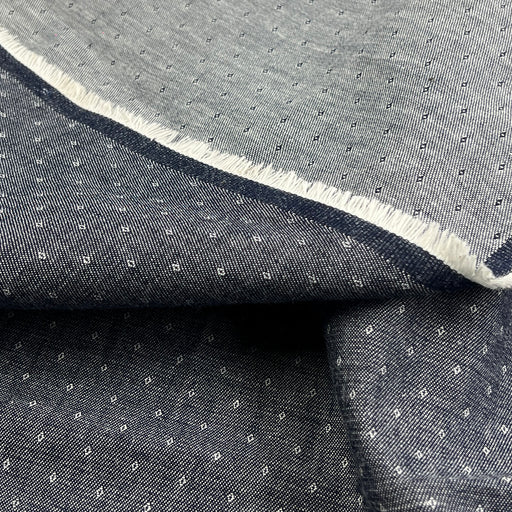 A close-up of folded dark gray fabric with a small repeating white geometric pattern and a contrasting white frayed edge.