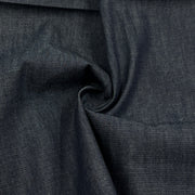 A close-up of dark indigo denim fabric with a textured twill weave, shown with a central swirl fold.