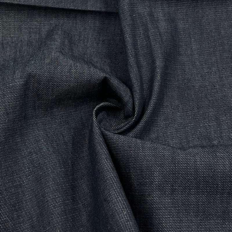A close-up of dark indigo denim fabric with a textured twill weave, shown with a central swirl fold.
