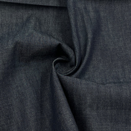 A close-up of dark indigo denim fabric with a textured twill weave, shown with a central swirl fold.