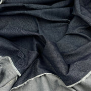 A close-up of draped dark indigo blue fabric with a visible woven texture and frayed white edges.
