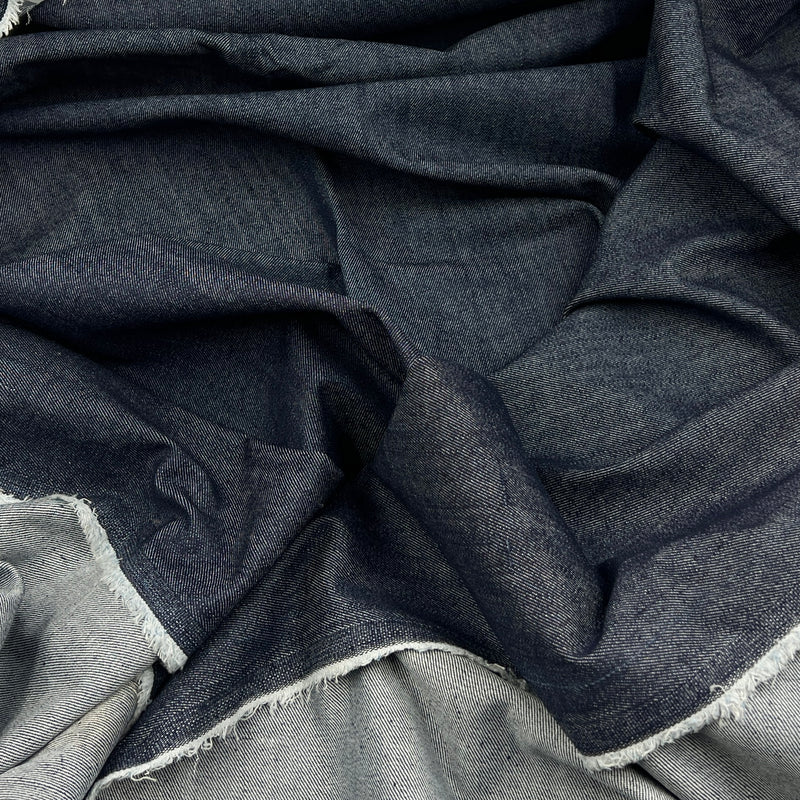 A close-up of draped dark indigo blue fabric with a visible woven texture and frayed white edges.