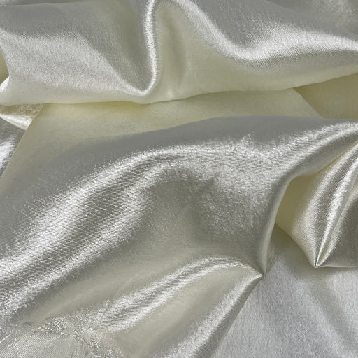 A close-up image of crepeback satin fabric in ivory color, showing its shiny satin face and textured reverse.