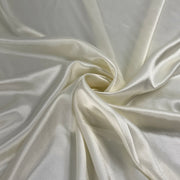 A close-up of draped satin fabric in a warm ivory or cream color, arranged in soft folds with a central swirl.