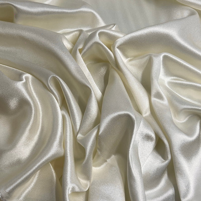 Close-up of draped satin fabric with soft folds and a subtle sheen, shown in a warm off-white or cream tone.