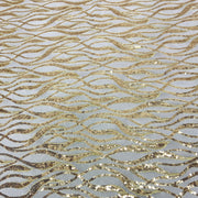 Gold sequined fabric with a wavy, flowing pattern on a light gray background.