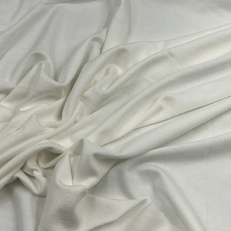 A close-up of draped off-white or cream-colored fabric with soft folds and a smooth texture.