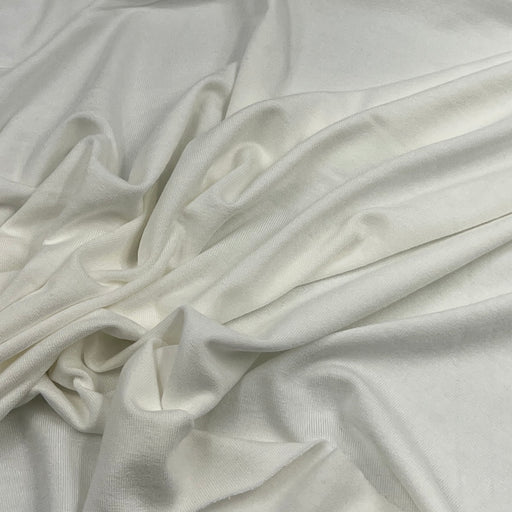 A close-up of draped off-white or cream-colored fabric with soft folds and a smooth texture.
