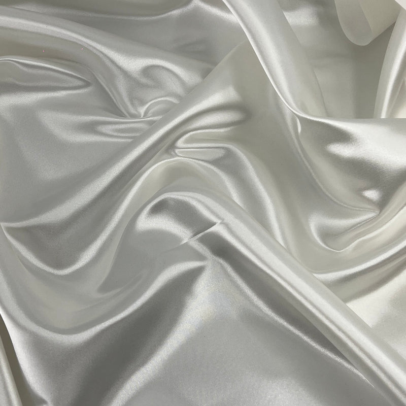 A close-up of draped satin fabric with a soft sheen, showing folds and a light warm gray to off-white color.