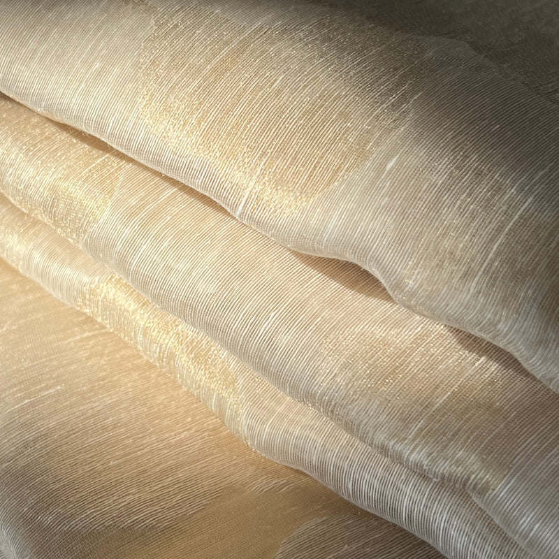 A close-up of draped champagne-colored fabric with a subtle textured sheen and fine ribbed lines.