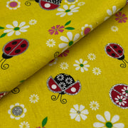 Yellow fabric with a repeating pattern of ladybugs and white daisies, folded diagonally to show the texture and print.