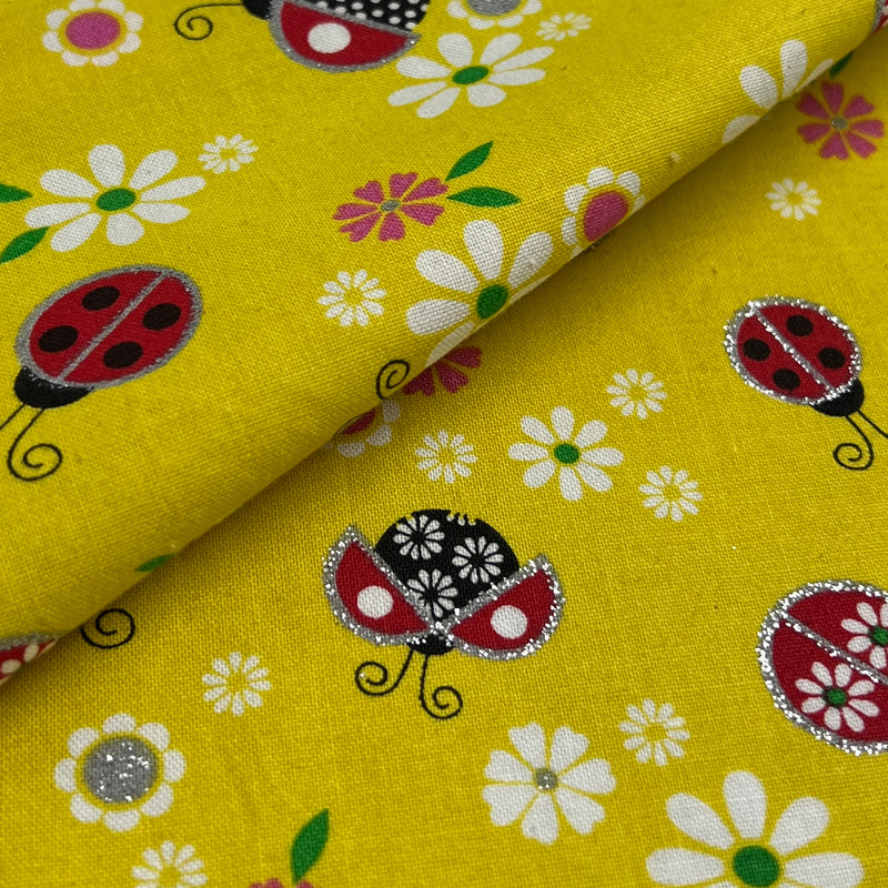 Yellow fabric with a repeating pattern of ladybugs and white daisies, folded diagonally to show the texture and print.