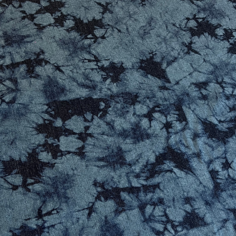 A close-up of a blue and navy tie-dye fabric with a textured, slightly fuzzy surface showing a starburst pattern.