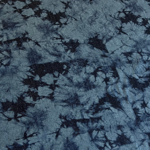A close-up of a blue and navy tie-dye fabric with a textured, slightly fuzzy surface showing a starburst pattern.