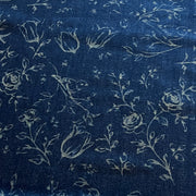 A close-up of dark indigo blue fabric with a light beige floral and bird print, showing roses, tulips, leaves, and small birds.