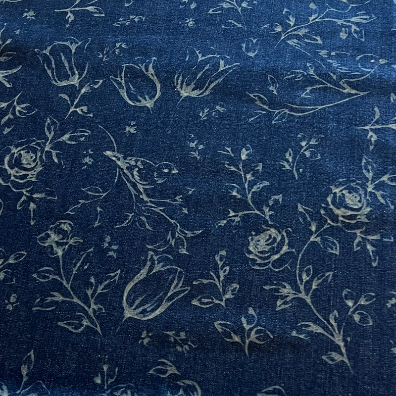 A close-up of dark indigo blue fabric with a light beige floral and bird print, showing roses, tulips, leaves, and small birds.