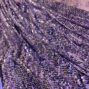 Close-up of a purple sequined fabric with shimmering lavender and silver tones, draped in soft folds.