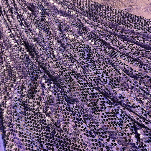Close-up of a purple sequined fabric with shimmering lavender and silver tones, draped in soft folds.
