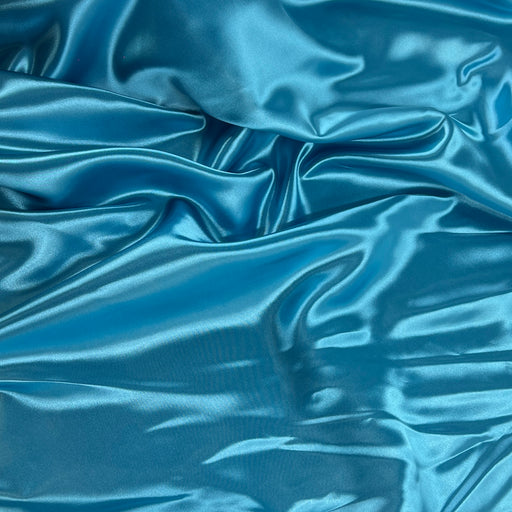 A close-up of shiny blue satin fabric with soft folds and a smooth, lustrous texture.