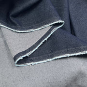 A close-up of folded dark indigo denim fabric with a raw, frayed selvedge edge showing the lighter inner weave.