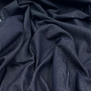 A close-up of draped dark indigo blue fabric with a subtle woven texture, showing soft folds and shadows.