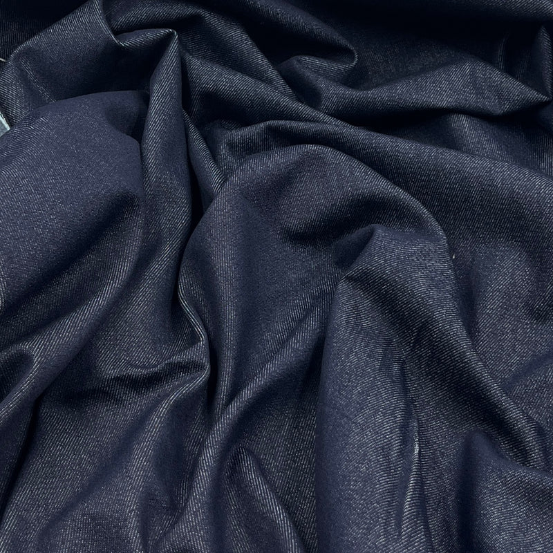 A close-up of draped dark indigo blue fabric with a subtle woven texture, showing soft folds and shadows.