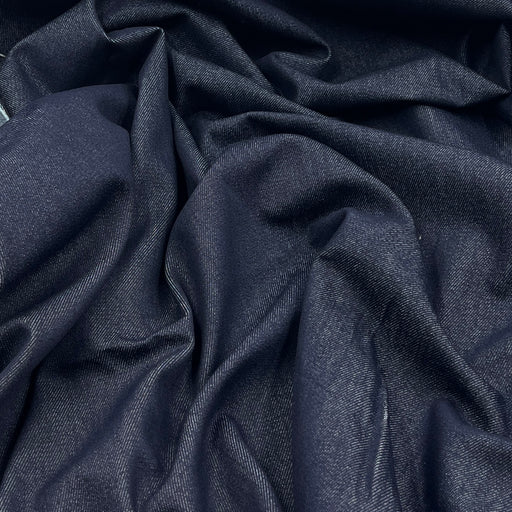 A close-up of draped dark indigo blue fabric with a subtle woven texture, showing soft folds and shadows.