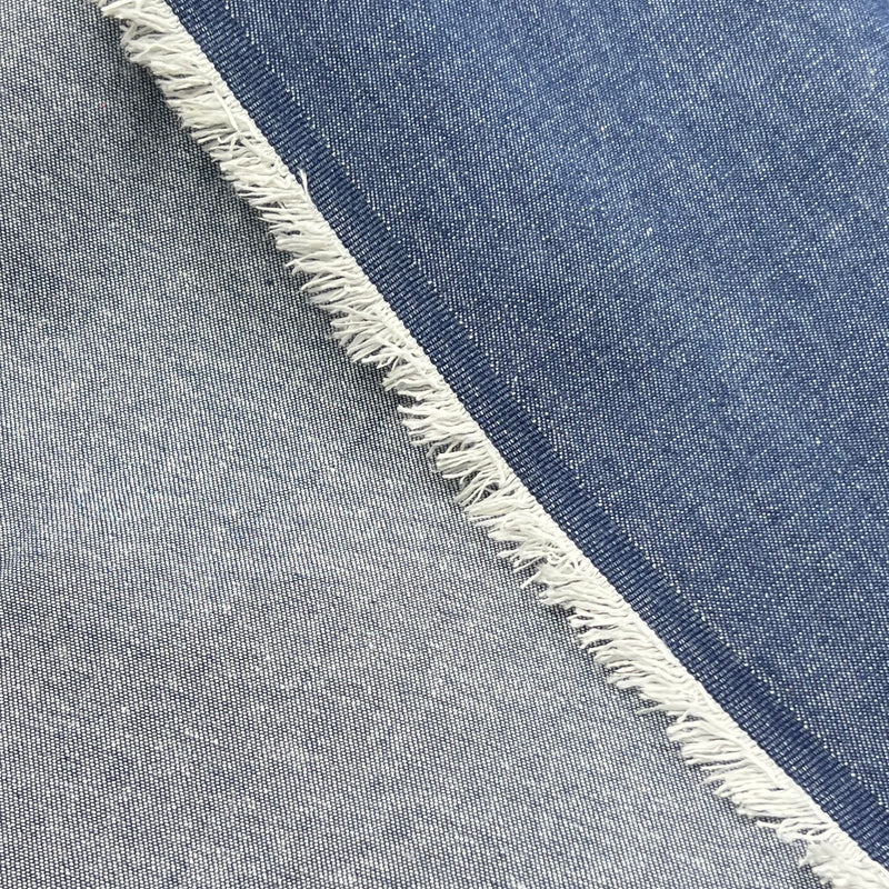 Close-up of the face and reverse of a blue denim fabric crossed diagonally, showing medium blue wash on one side and one in light gray wash, with a frayed edge visible between them.