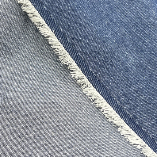 Close-up of the face and reverse of a blue denim fabric crossed diagonally, showing medium blue wash on one side and one in light gray wash, with a frayed edge visible between them.