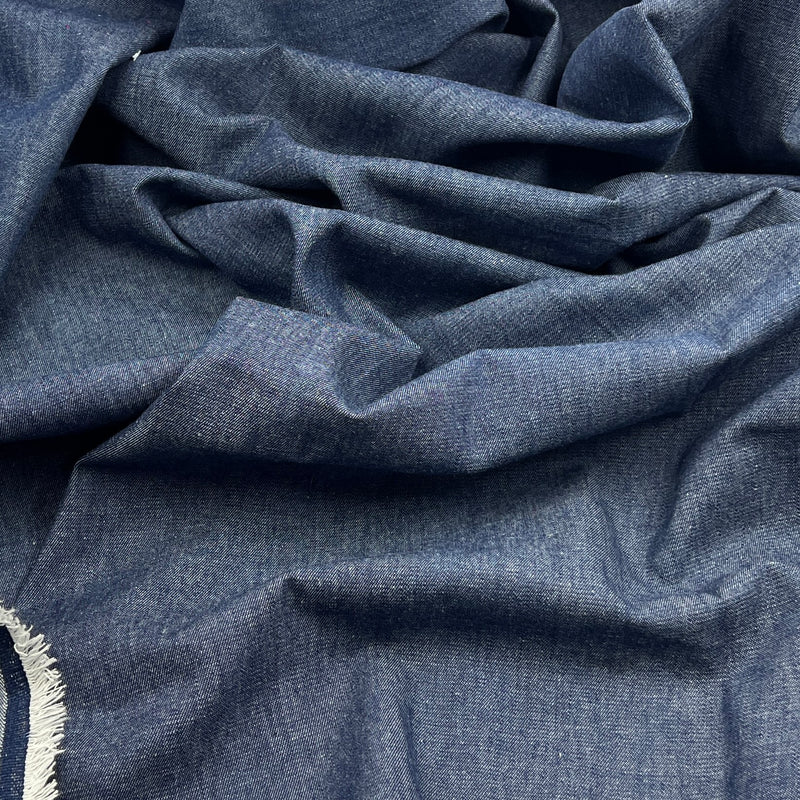 A close-up of draped blue fabric with a fine woven texture and a small section of white fringe visible at the lower left edge.