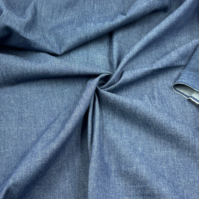 A close-up of draped blue denim fabric with a twisted center, showing its textured weave and a small hem detail on the right side.