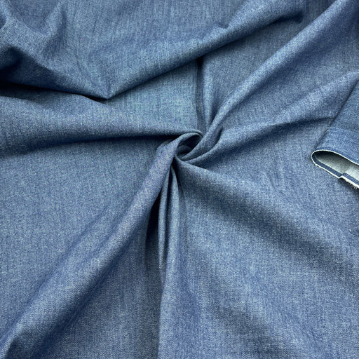 A close-up of draped blue denim fabric with a twisted center, showing its textured weave and a small hem detail on the right side.