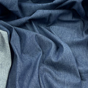 A close-up of draped blue fabric with a fine textured weave, showing soft folds and shadows across the material.