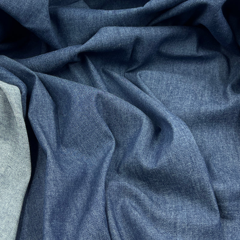 A close-up of draped blue fabric with a fine textured weave, showing soft folds and shadows across the material.